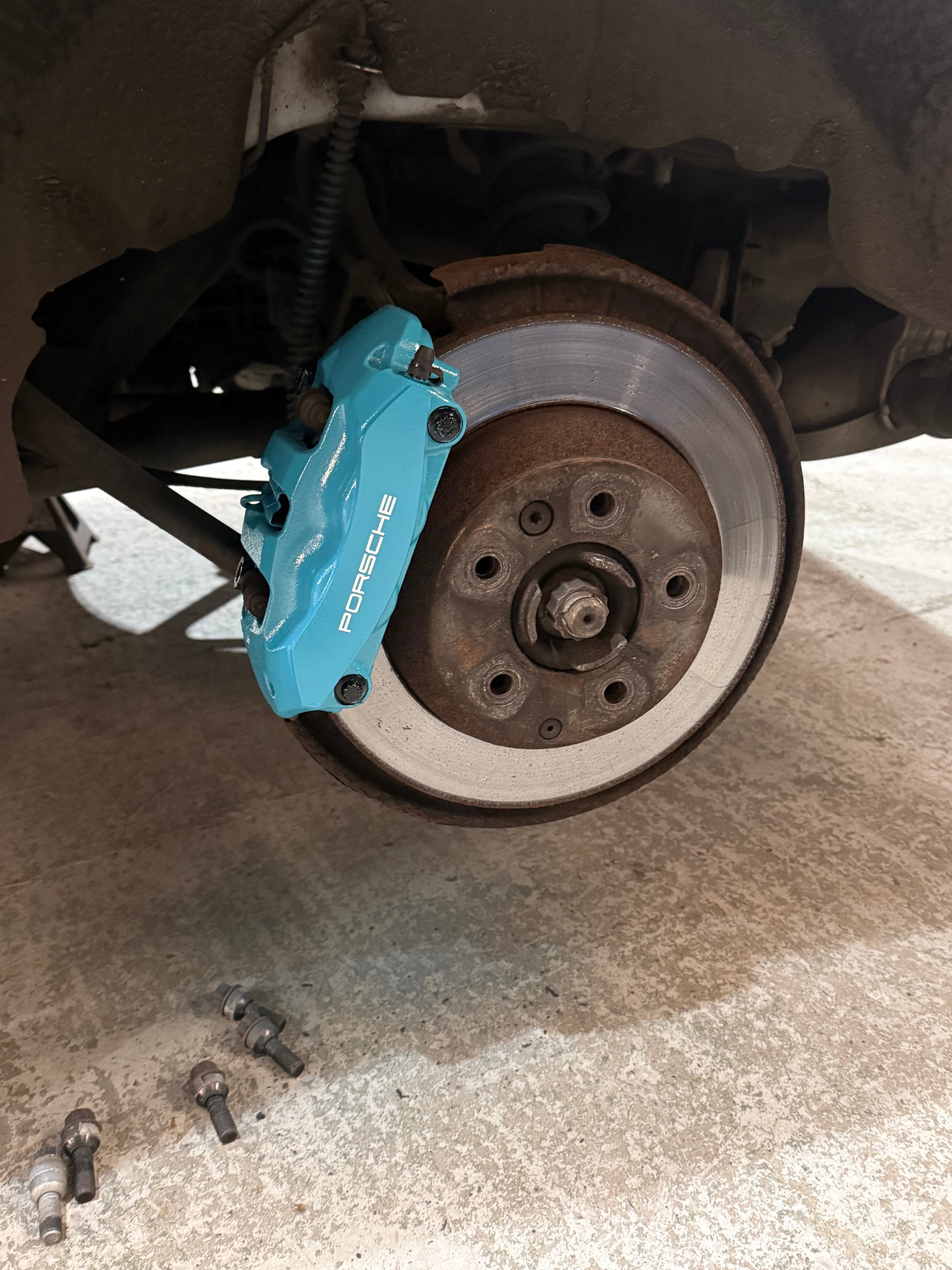 Porsche front brake caliper before painting, showing worn grey finish — after painting in blue