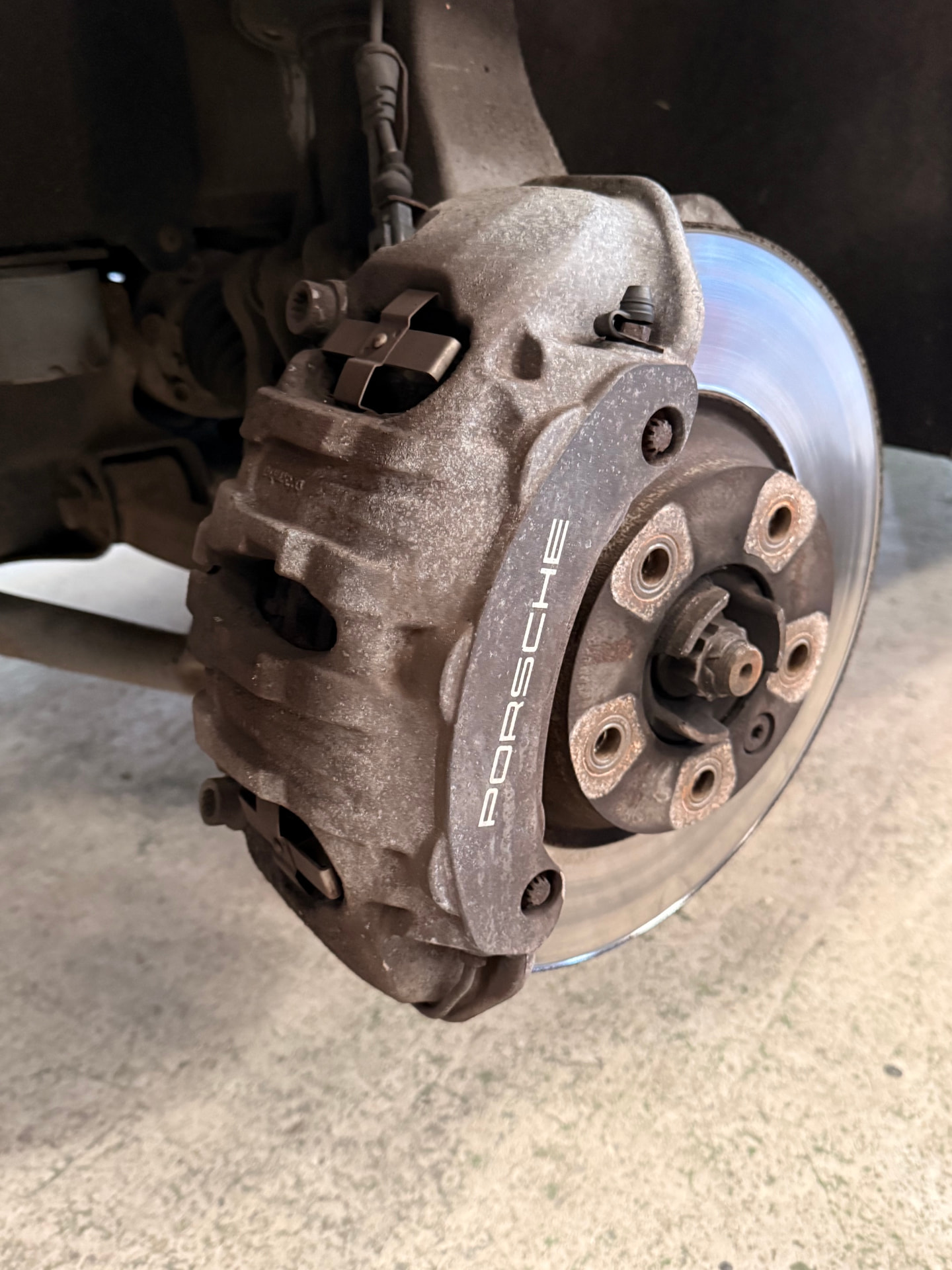 Porsche front brake caliper before painting, showing worn grey finish