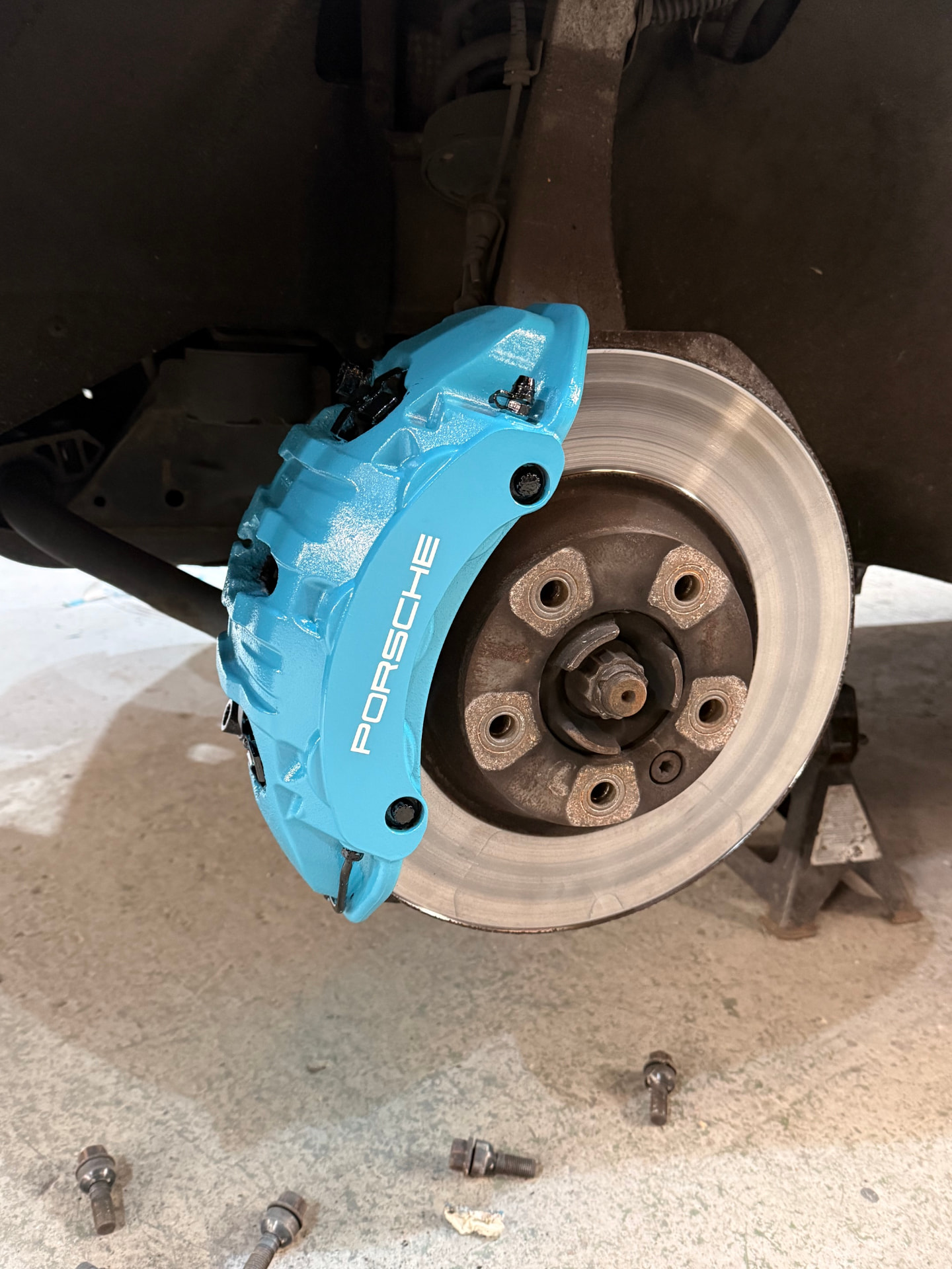 Porsche rear brake caliper before painting, showing corroded grey finish — after painting in blue